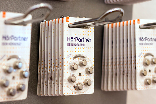 Hörgerätebatterien von HörPartner in Blisterverpackungen hängen an einer Ladenwand.